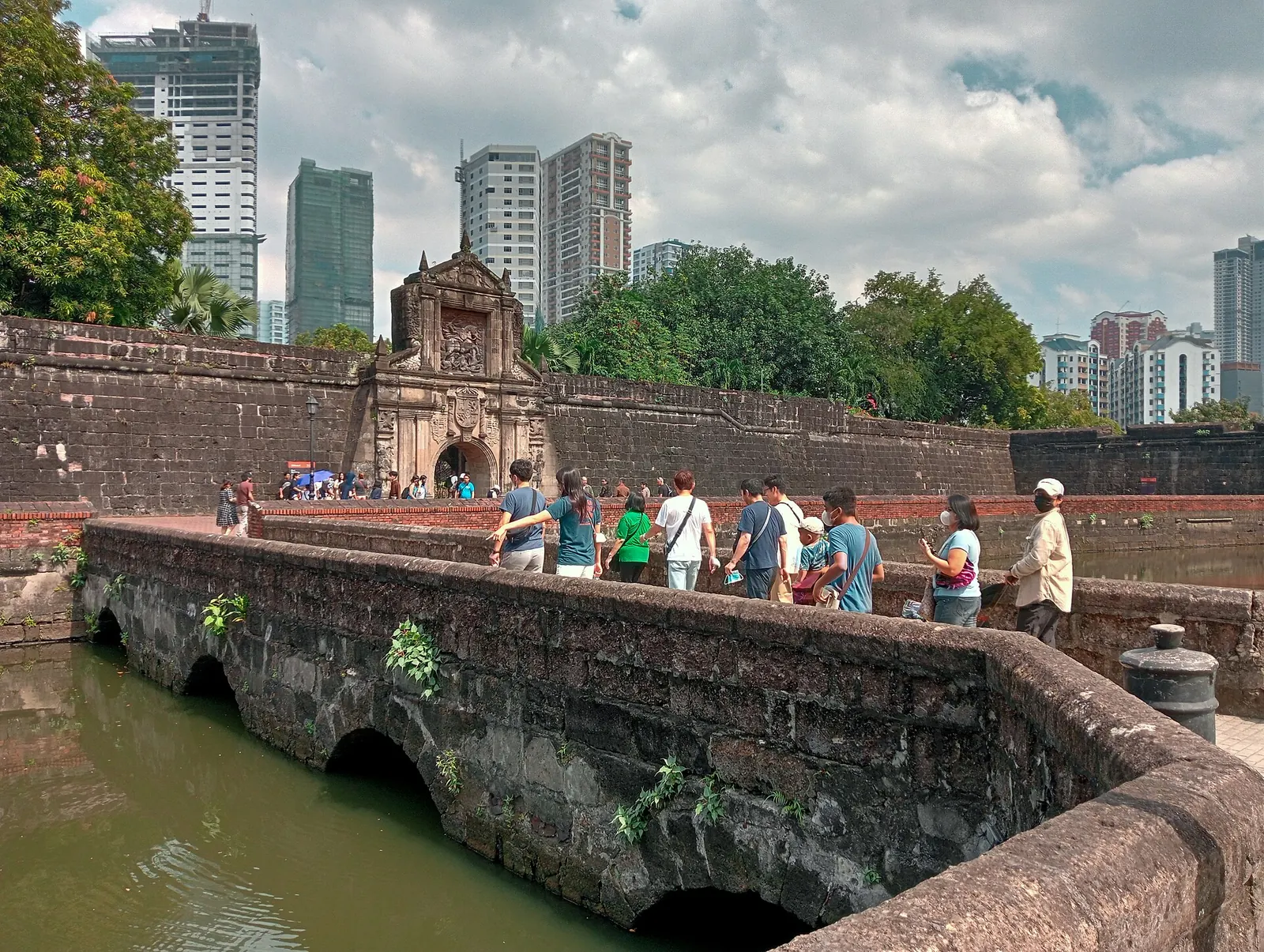A stone bridge leading toward Fort Santiago in Intramuros, with visitors and Manila buildings beyond.